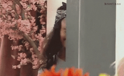 A Woman Is Standing In Front Of A Cherry Blossom Tree And Looking Out Of A Window . GIF