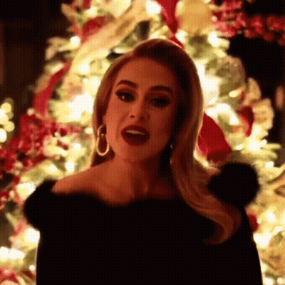 A Woman Is Standing In Front Of A Christmas Tree And Singing . GIF