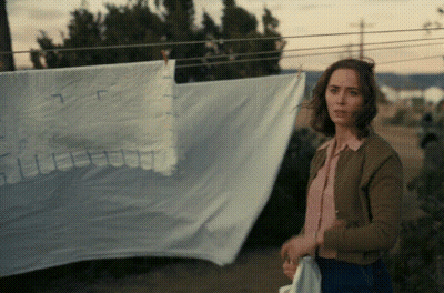 A Woman Is Standing In Front Of A Clothesline With A White Cloth Hanging On It GIF