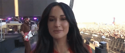 A Woman Is Standing In Front Of A Crowd While A Man Plays A Guitar GIF