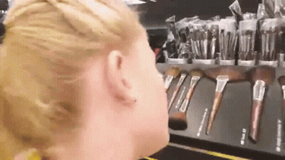 A Woman Is Standing In Front Of A Display Of Makeup Brushes GIF