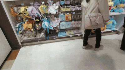 A Woman Is Standing In Front Of A Display Of Stuffed Animals Including One That Says Eevee GIF