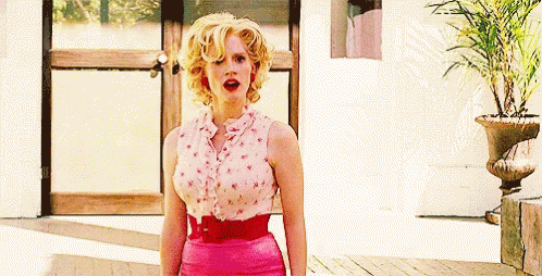 A Woman Is Standing In Front Of A Door Wearing A Pink Skirt And A Pink Shirt . GIF
