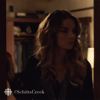 A Woman Is Standing In Front Of A Door With #Schitts Creek Written On The Bottom GIF