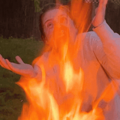 A Woman Is Standing In Front Of A Fire With Flames Coming Out Of Her Face GIF