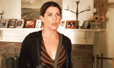 A Woman Is Standing In Front Of A Fireplace In A Living Room With Pictures On The Wall . GIF