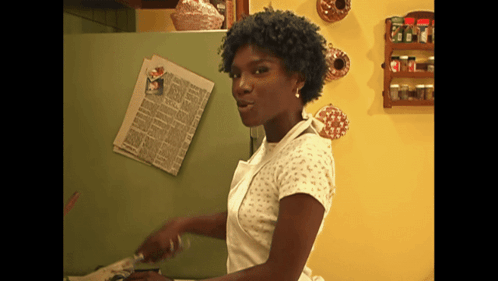A Woman Is Standing In Front Of A Green Refrigerator With A Newspaper On The Door GIF