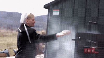 A Woman Is Standing In Front Of A Green Shed With Smoke Coming Out Of It .. GIF