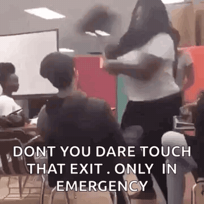 A Woman Is Standing In Front Of A Group Of People In A Classroom While A Man Sits In A Chair . GIF