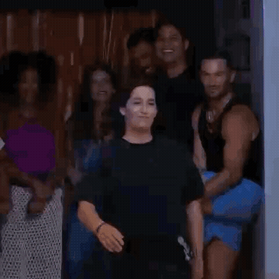 A Woman Is Standing In Front Of A Group Of People In A Doorway . GIF