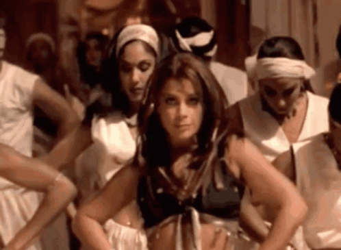 A Woman Is Standing In Front Of A Group Of Women Dancing In A Room . GIF