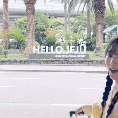 A Woman Is Standing In Front Of A Hello Jeju Sign GIF
