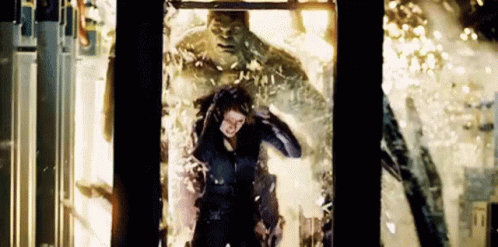 A Woman Is Standing In Front Of A Hulk In A Glass Box . GIF
