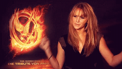 A Woman Is Standing In Front Of A Hunger Games Poster GIF