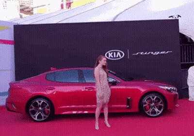 A Woman Is Standing In Front Of A Kia Advertisement GIF