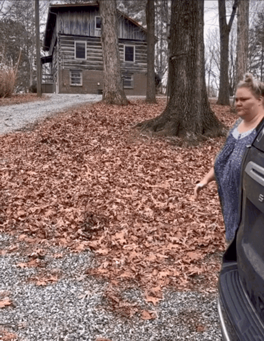 A Woman Is Standing In Front Of A Log Cabin In The Woods GIF