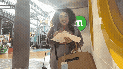 A Woman Is Standing In Front Of A M & M Sign GIF