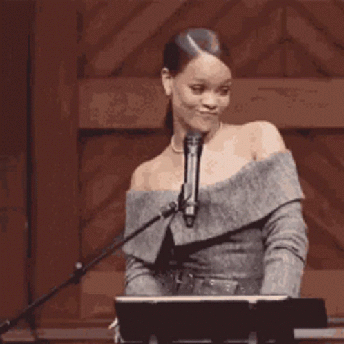 A Woman Is Standing In Front Of A Microphone And A Piano . GIF