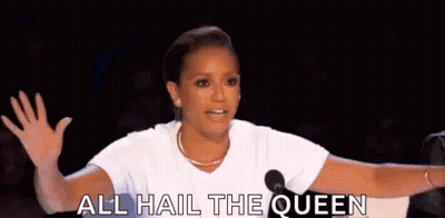 a woman is standing in front of a microphone and saying `` all hail the queen '' while waving her hand .