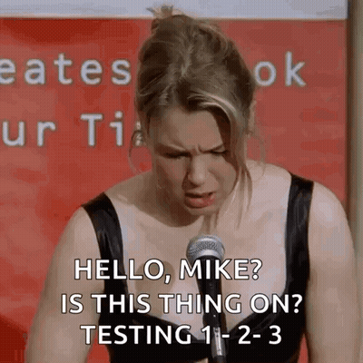A Woman Is Standing In Front Of A Microphone And Saying Hello , Mike ? Is This Thing On ? Testing 1-2-3 GIF