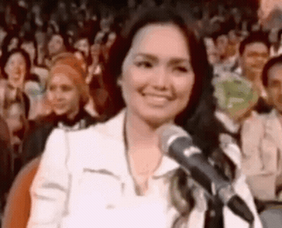 A Woman Is Standing In Front Of A Microphone And Smiling . GIF