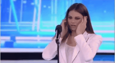 A Woman Is Standing In Front Of A Microphone Covering Her Ears . GIF
