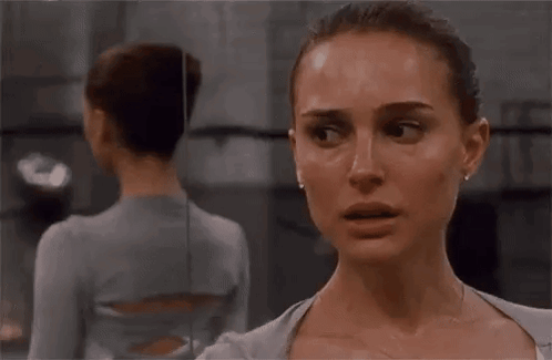 A Woman Is Standing In Front Of A Mirror And Looking At Herself . GIF