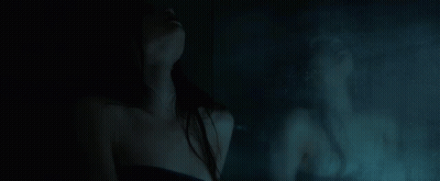 A Woman Is Standing In Front Of A Mirror In A Dark Room With Her Reflection In The Mirror . GIF