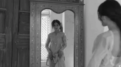 A Woman Is Standing In Front Of A Mirror Looking At Her Reflection . GIF