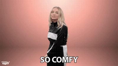 A Woman Is Standing In Front Of A Pink Background With The Words So Comfy Written On It GIF
