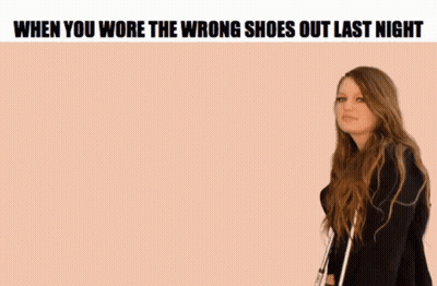 A Woman Is Standing In Front Of A Pink Background With The Words `` When You Wore The Wrong Shoes Out Last Night '' On I GIF
