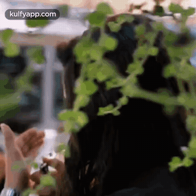 A Woman Is Standing In Front Of A Plant With Leaves On Her Hair . GIF