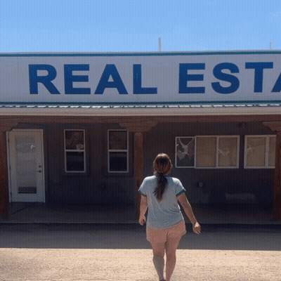 A Woman Is Standing In Front Of A Real Estate Sign GIF