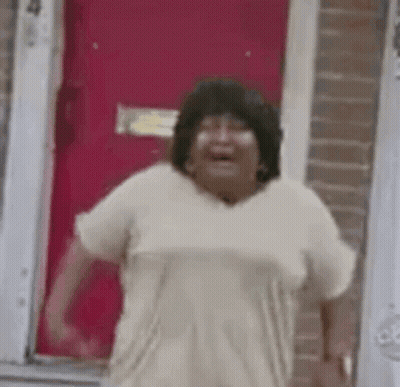 A Woman Is Standing In Front Of A Red Door Laughing . GIF