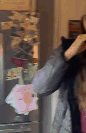 A Woman Is Standing In Front Of A Refrigerator Holding A Piece Of Paper GIF