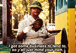 A Woman Is Standing In Front Of A School Bus Holding A Tray Of Food And A Book GIF
