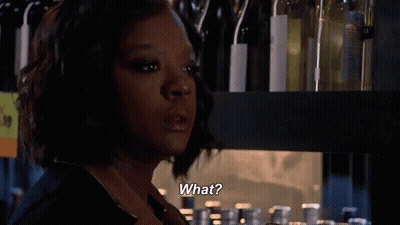 A Woman Is Standing In Front Of A Shelf With Wine Bottles And Says What . GIF
