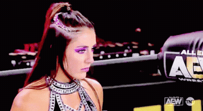 A Woman Is Standing In Front Of A Sign That Says Aew On It GIF