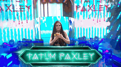A Woman Is Standing In Front Of A Sign That Says Tatum Paxley On It . GIF