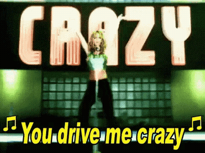 A Woman Is Standing In Front Of A Sign That Says `` You Drive Me Crazy '' While Holding A Microphone . GIF