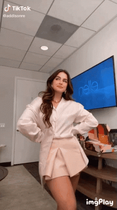 A Woman Is Standing In Front Of A Television With The Name Addisonre On It GIF