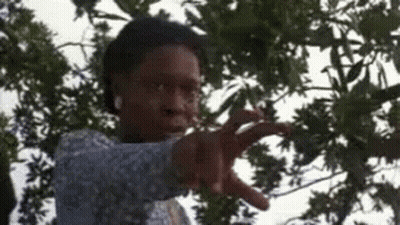 A Woman Is Standing In Front Of A Tree And Pointing At The Camera . GIF