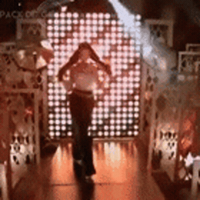 A Woman Is Standing In Front Of A Wall Of Lights In A Dark Room . GIF