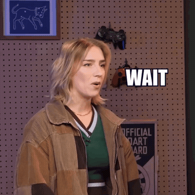 A Woman Is Standing In Front Of A Wall That Says Wait Wait GIF