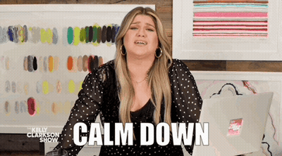 A Woman Is Standing In Front Of A Wall With Paintings And Says Calm Down GIF