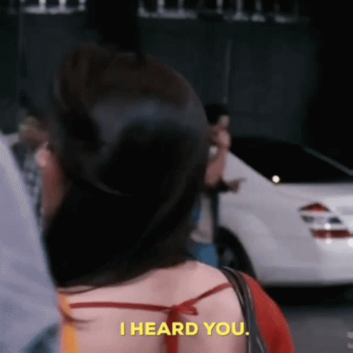 A Woman Is Standing In Front Of A White Car And Saying `` I Heard You . '' GIF