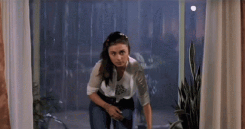 A Woman Is Standing In Front Of A Window Looking Out GIF
