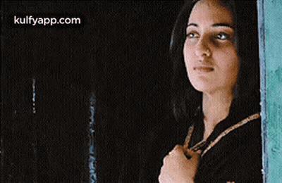 A Woman Is Standing In Front Of A Window Looking Out . GIF