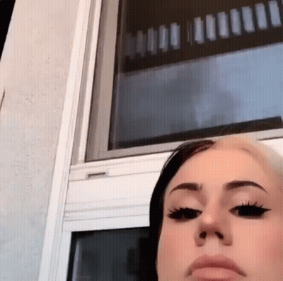 A Woman Is Standing In Front Of A Window With A Reflection Of A Building In The Window . GIF