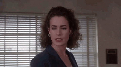 A Woman Is Standing In Front Of A Window With Blinds . GIF